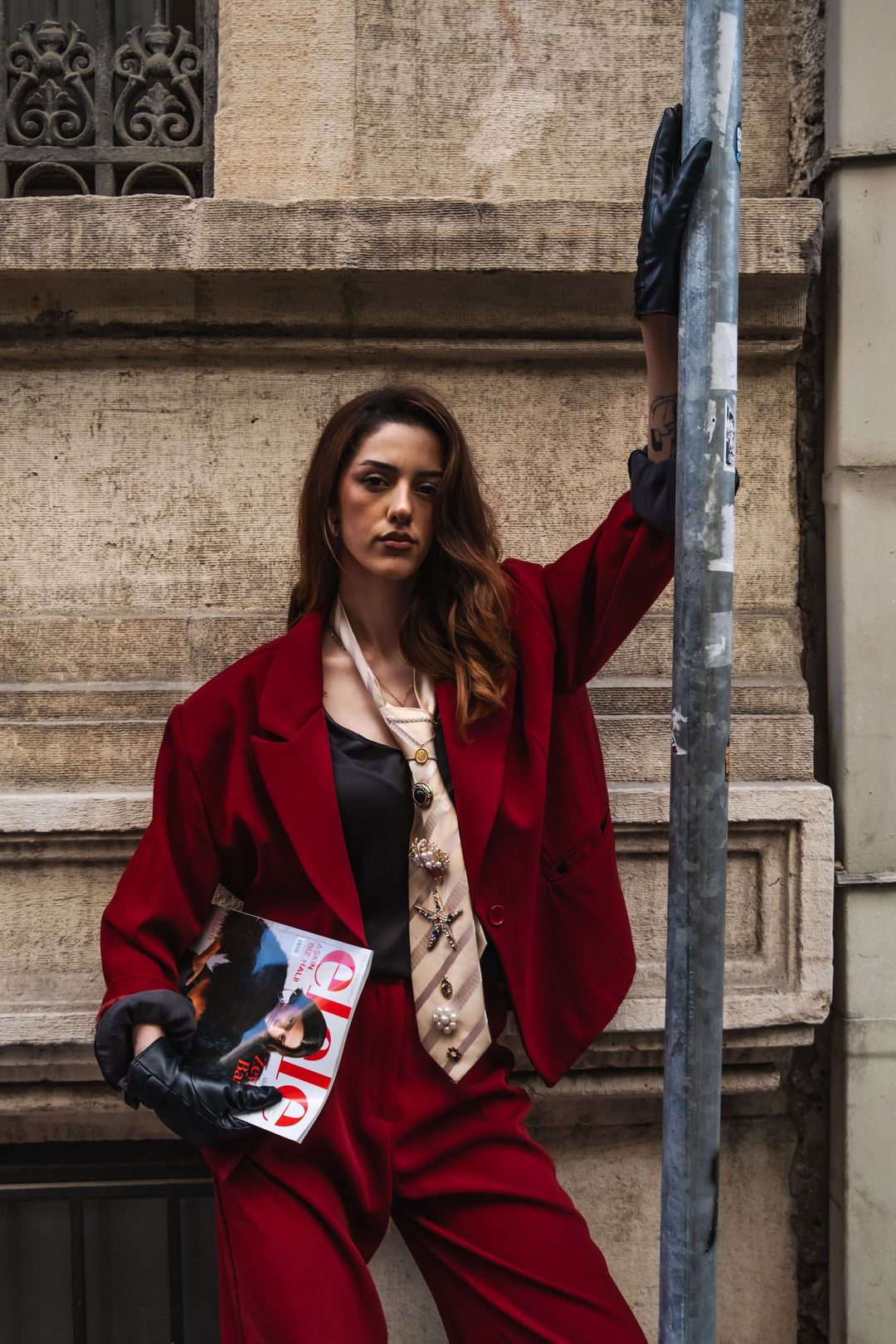 Model in an oxblood blazer and printed tie, leaning on a stone facade